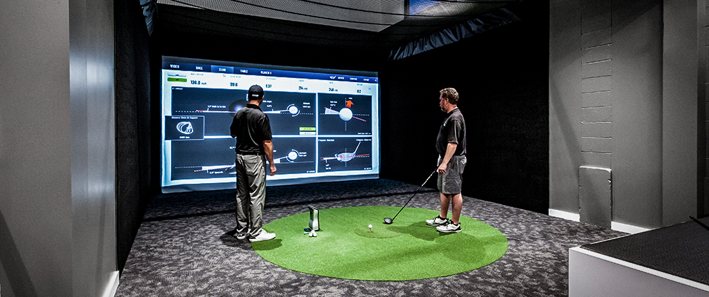 A golfer and fitter reviewing launch monitor data on a large screen
